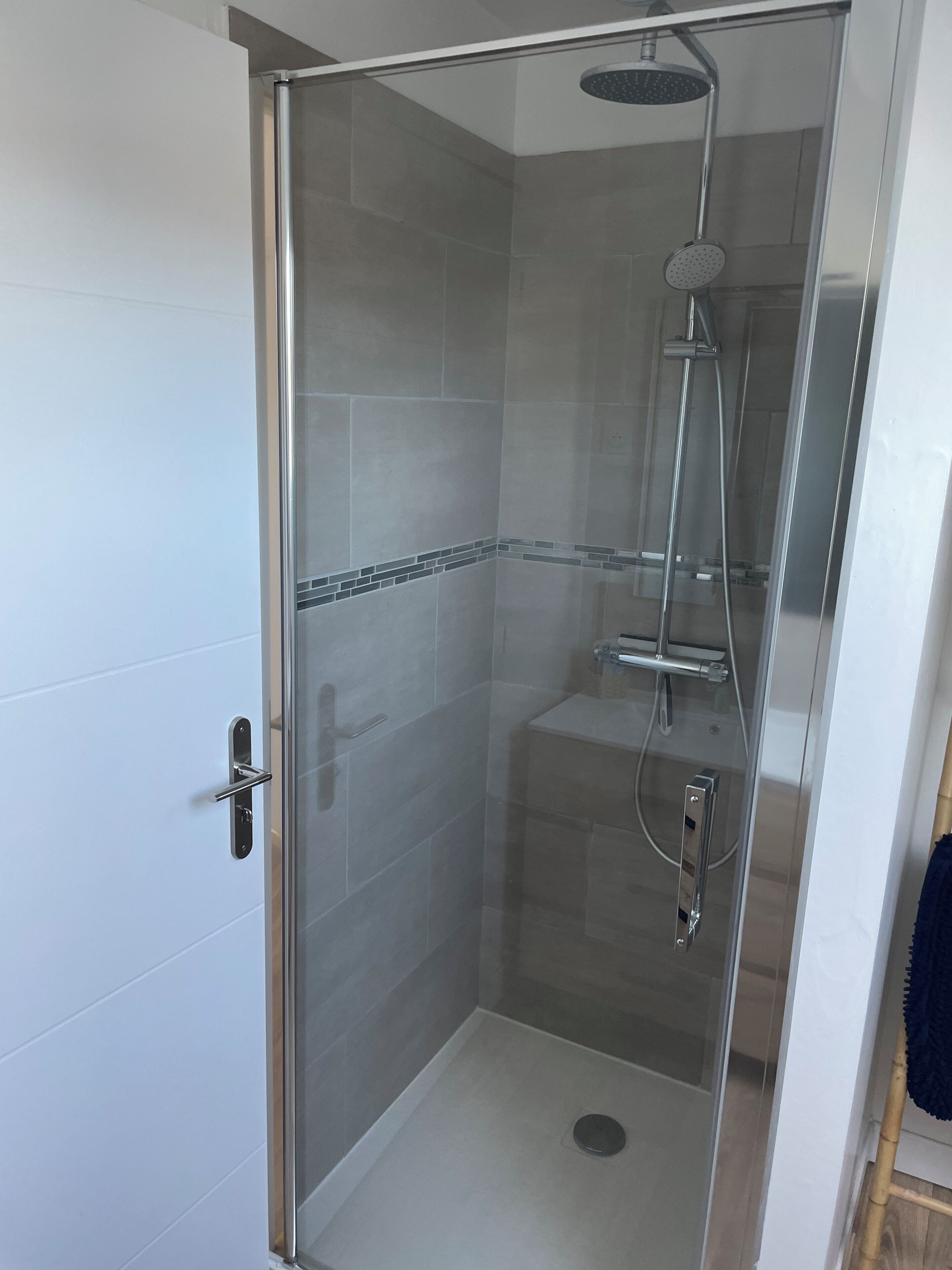 Une cabine de douche fermée par des parois en verre, dotée d’un pommeau de douche à main, d’un robinet mural et d’un drain au sol.