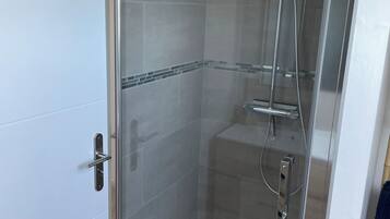 Une cabine de douche fermée par des parois en verre, dotée d’un pommeau de douche à main, d’un robinet mural et d’un drain au sol.