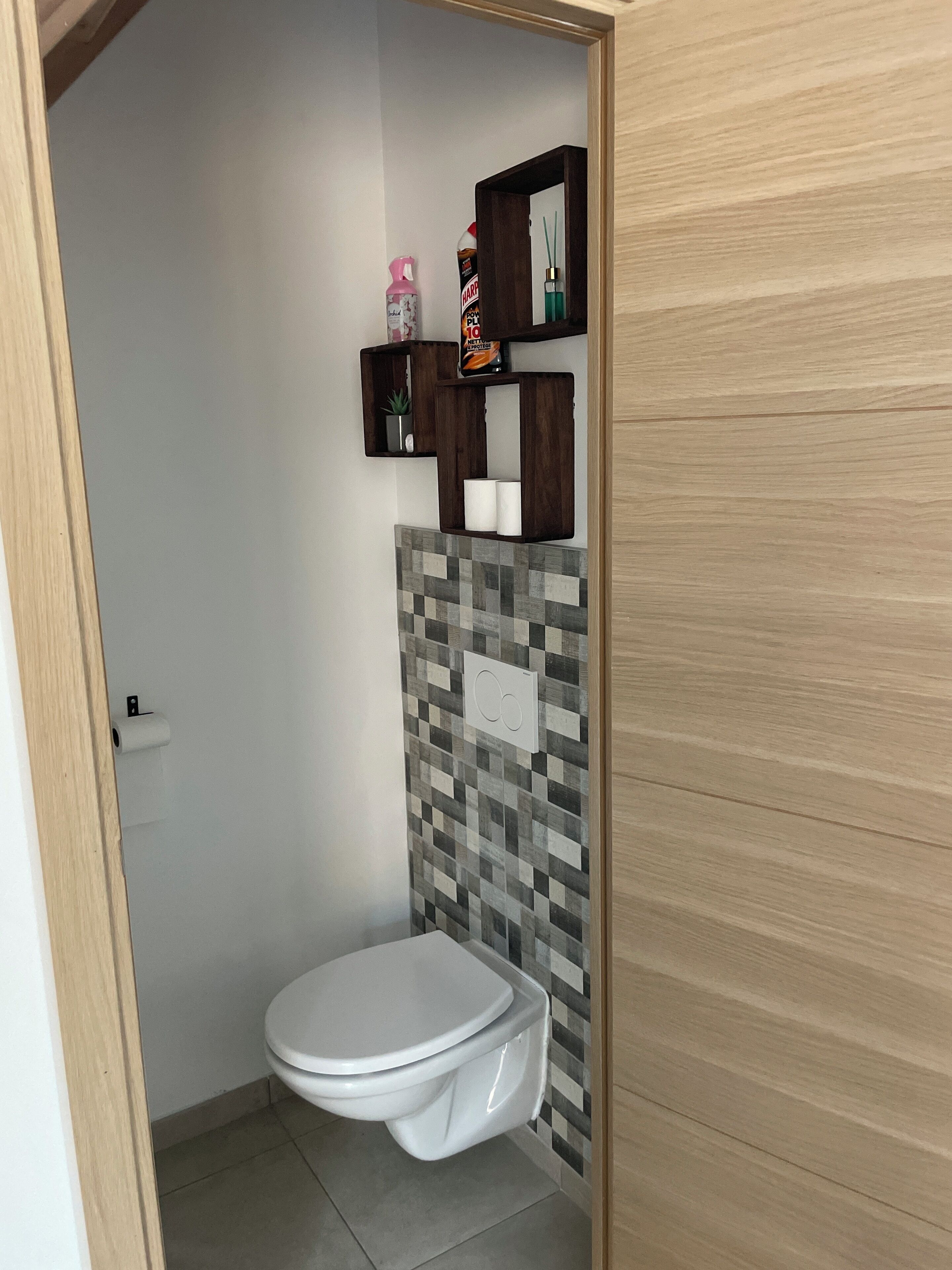 Et lille badeværelse med toilet, en hylde med toiletartikler og et flisebordsdragt.