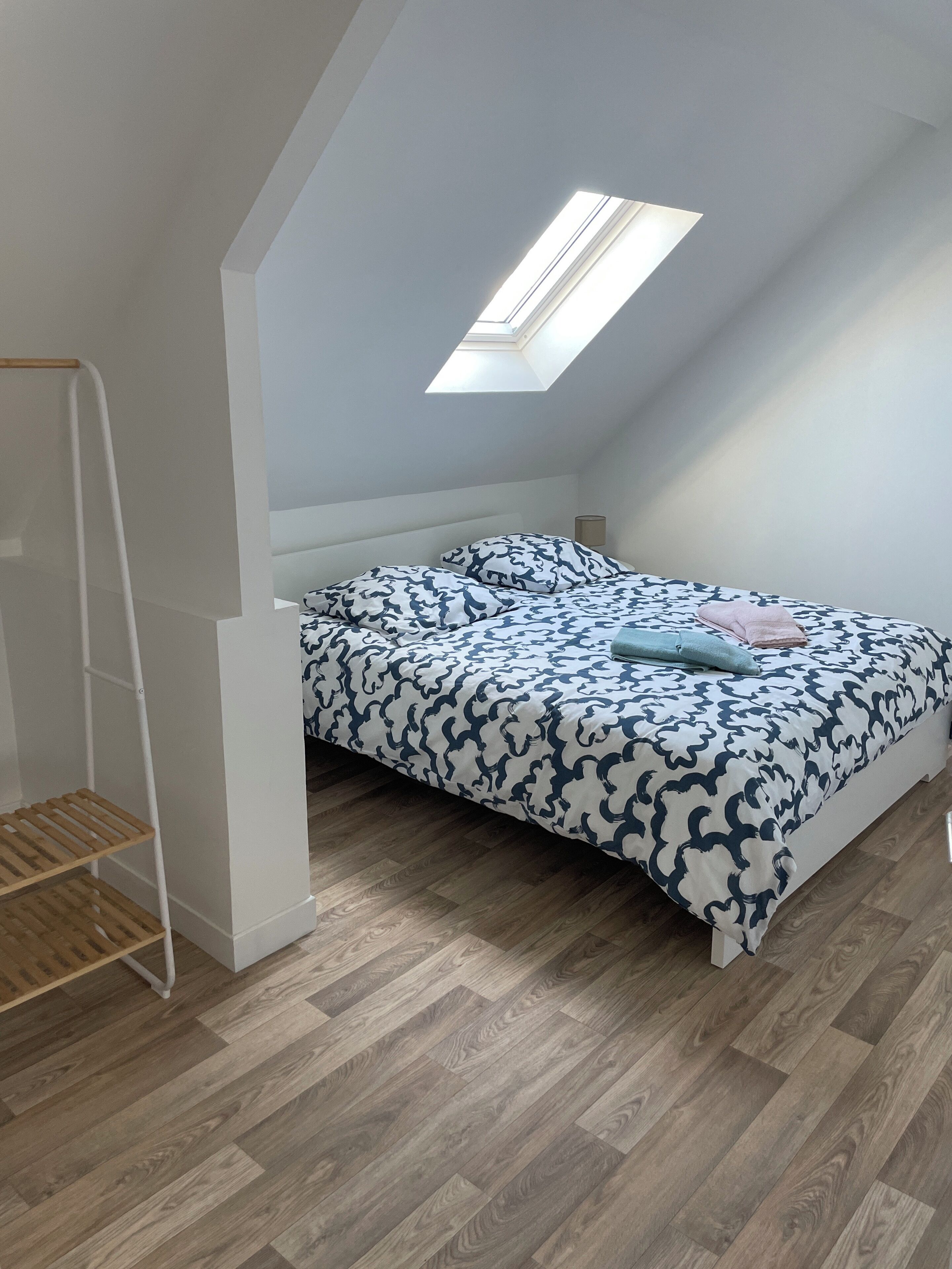 Camera da letto con soffitto a falde, un lucernario, un letto con lenzuola fantasia e pavimento in legno.