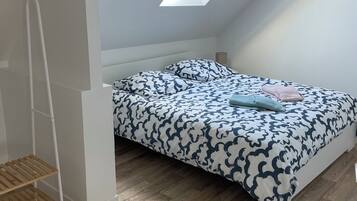 Camera da letto con soffitto a falde, un lucernario, un letto con lenzuola fantasia e pavimento in legno.