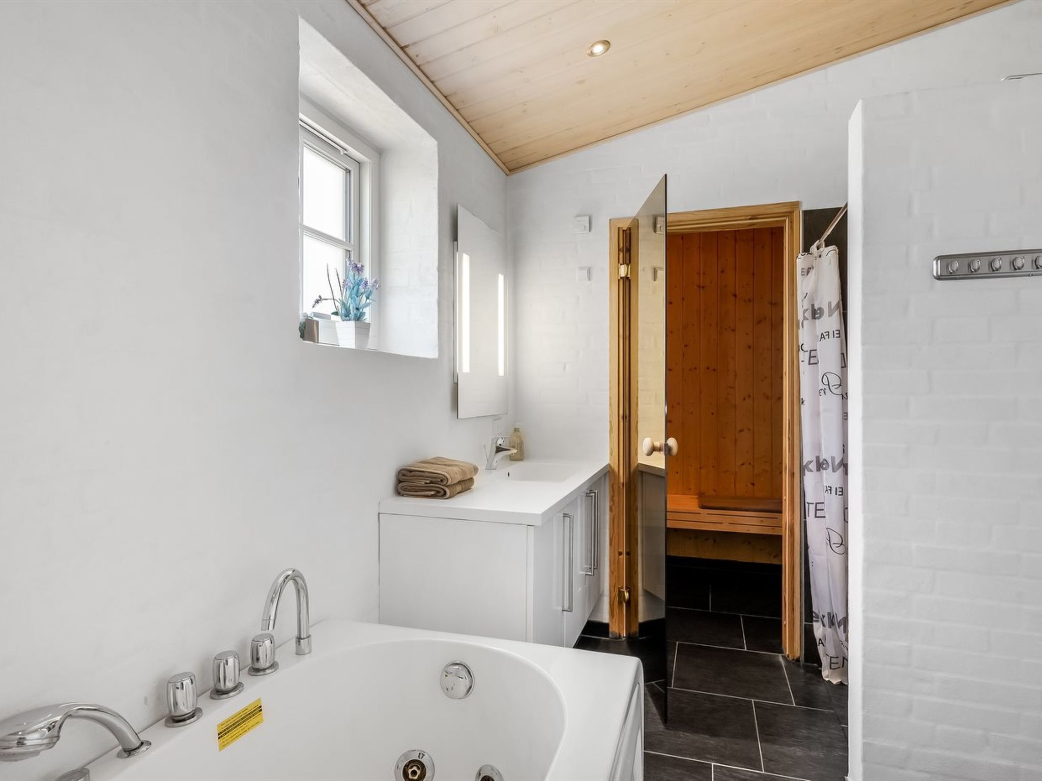 Une salle de bain moderne avec une grande baignoire, un lavabo doté de plusieurs robinets et une porte en bois donnant sur une autre pièce.