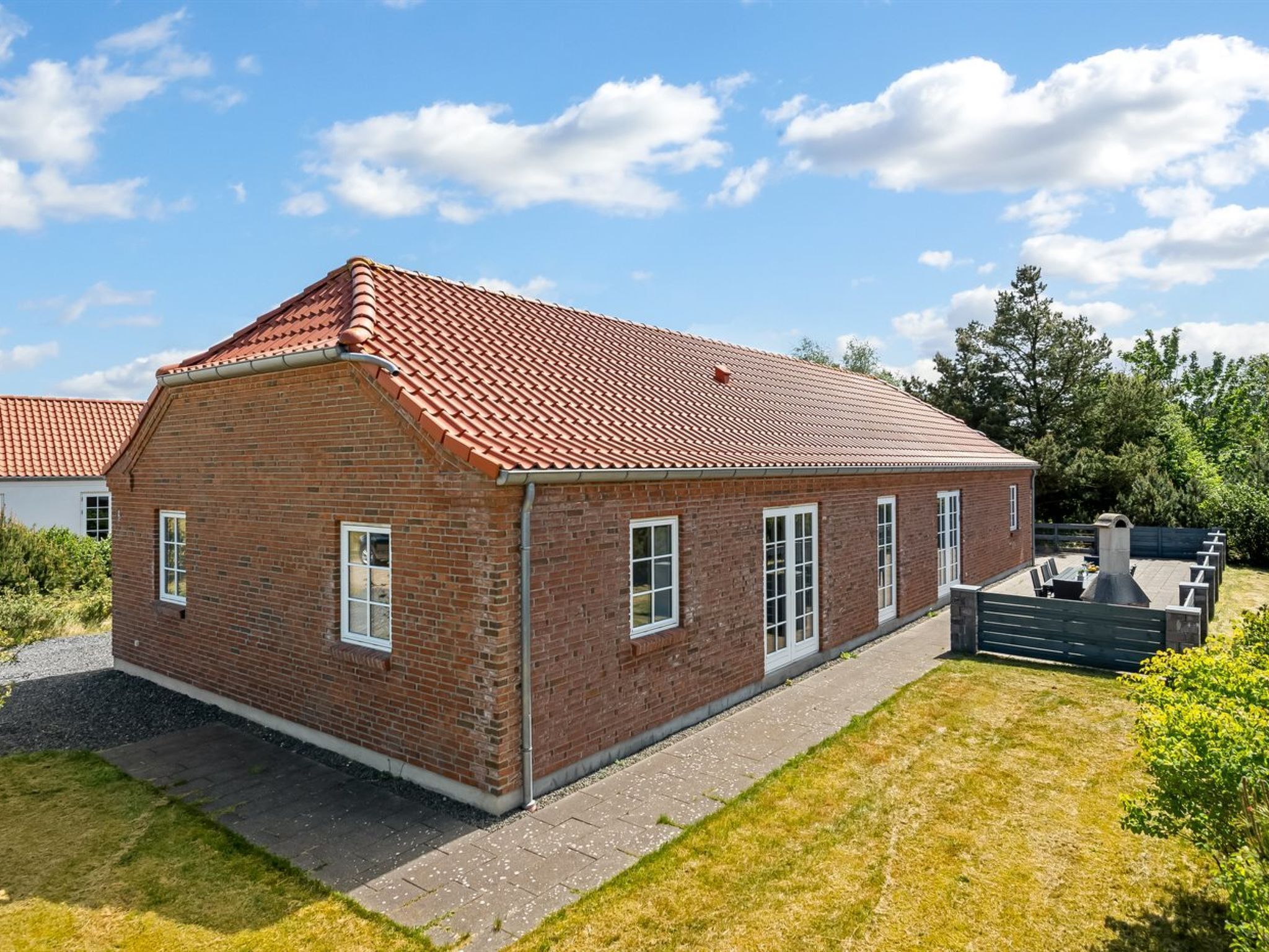 A single-story brick house with a red-tiled roof, a paved driveway, and a small garden area.