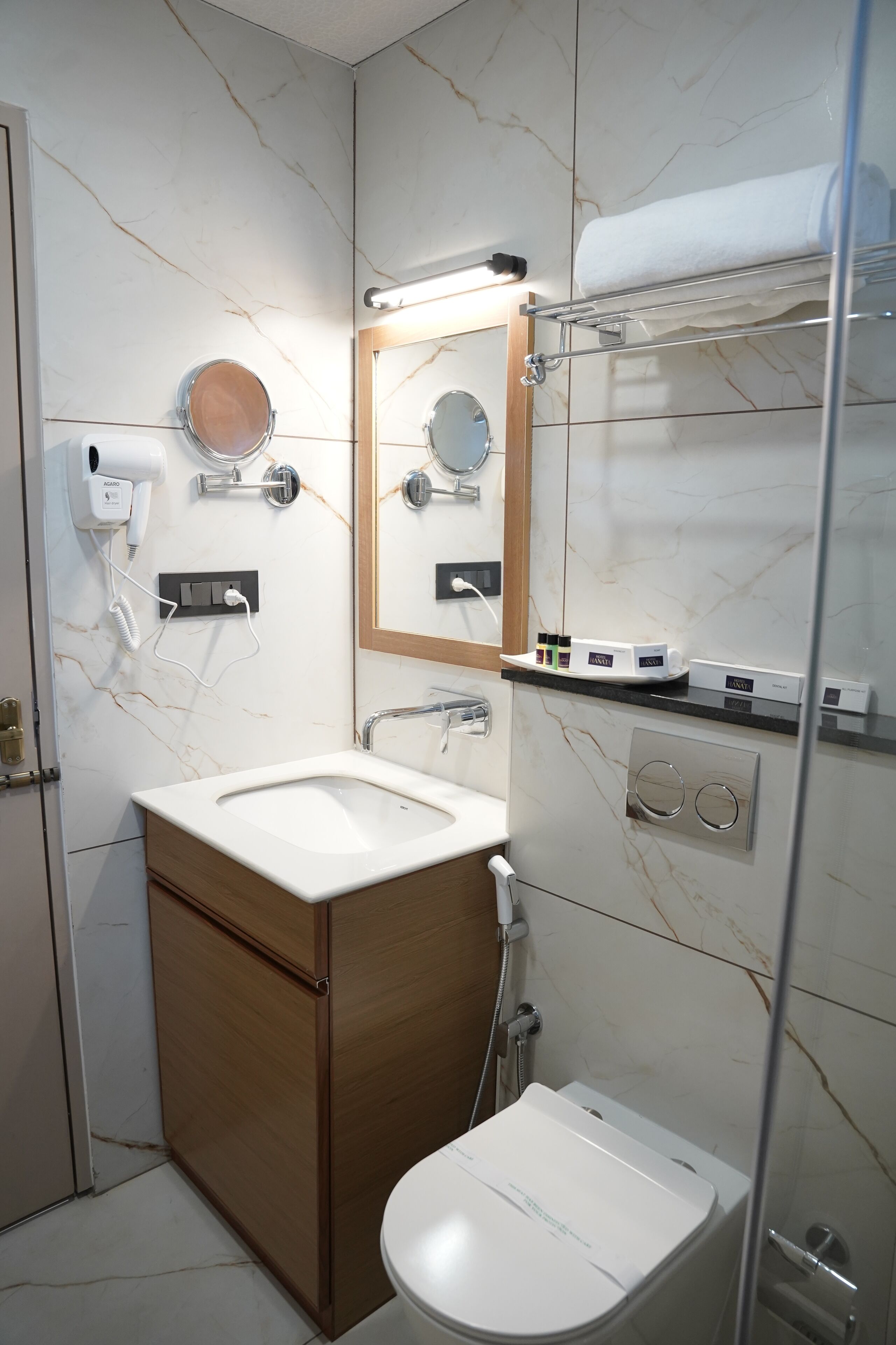 A bathroom with a marble wall, a sink, a mirror, a towel rack, and a toilet.