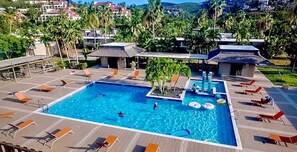 A large outdoor swimming pool with multiple lanes, surrounded by lounge chairs and umbrellas, set against a backdrop of palm trees and buildings. - Beautiful 3BR/4BA villa footsteps from beach (St. Thomas)