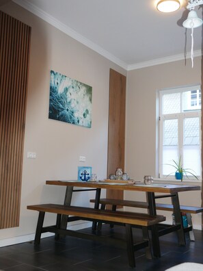 A dining area with a wooden table and benches, a wall-mounted painting, and a window with blinds. - Fully renovated ground-floor apartment in the heart of Goslar's Old Town (Goslar)