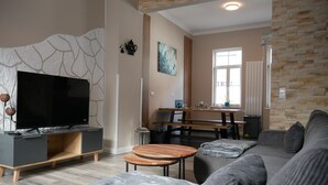 Een moderne woonkamer met een grote flatscreen-tv, een grijze bank, een houten salontafel en een accentmuur van steen.