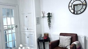 Ein Wohnzimmer mit einem braunen Ledersessel, einem Holztisch mit Dekoration, einer Wanduhr und einer weißen Tür mit Fenster.