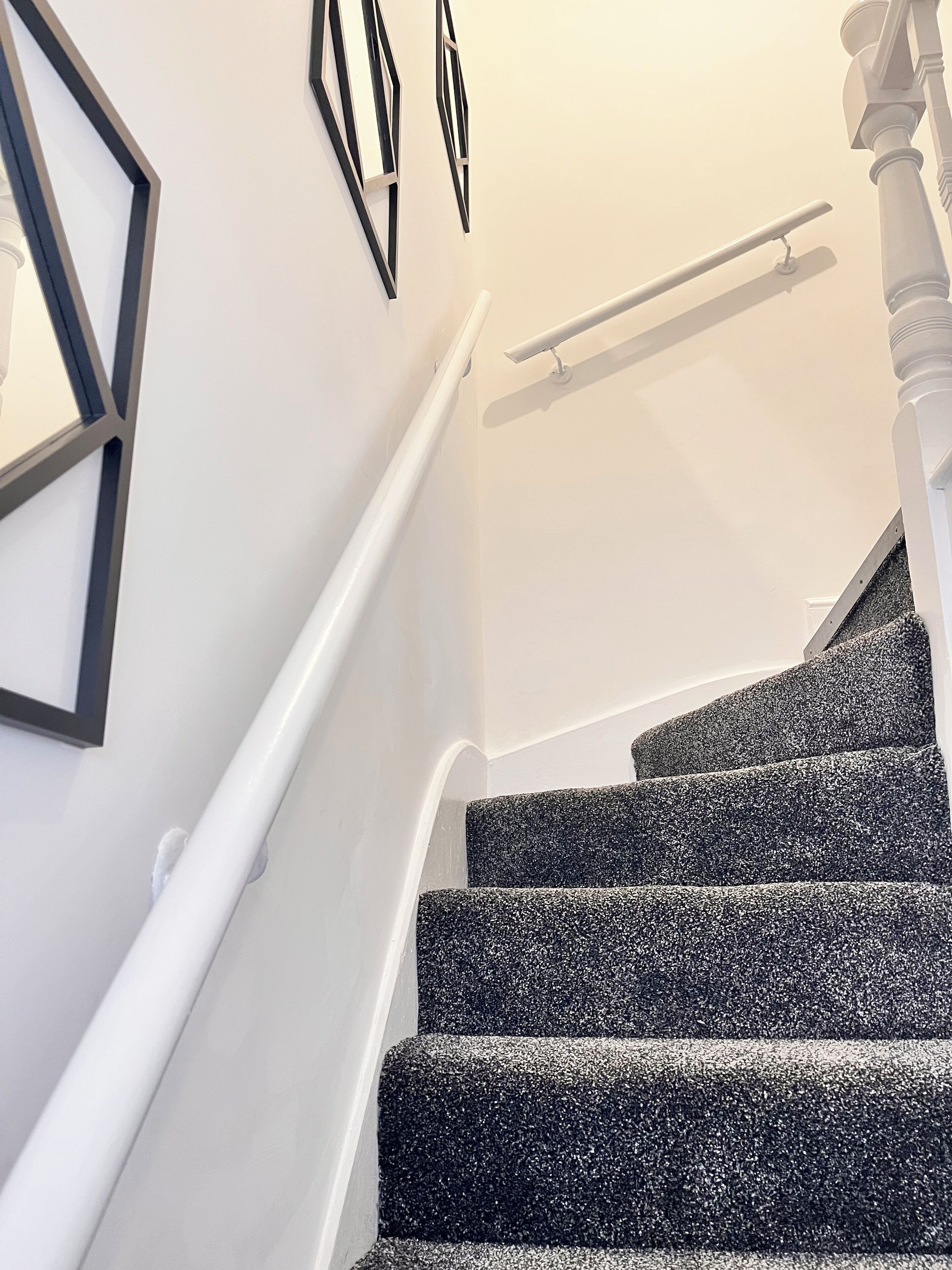 A staircase with a handrail, carpeted steps, and wall-mounted picture frames.