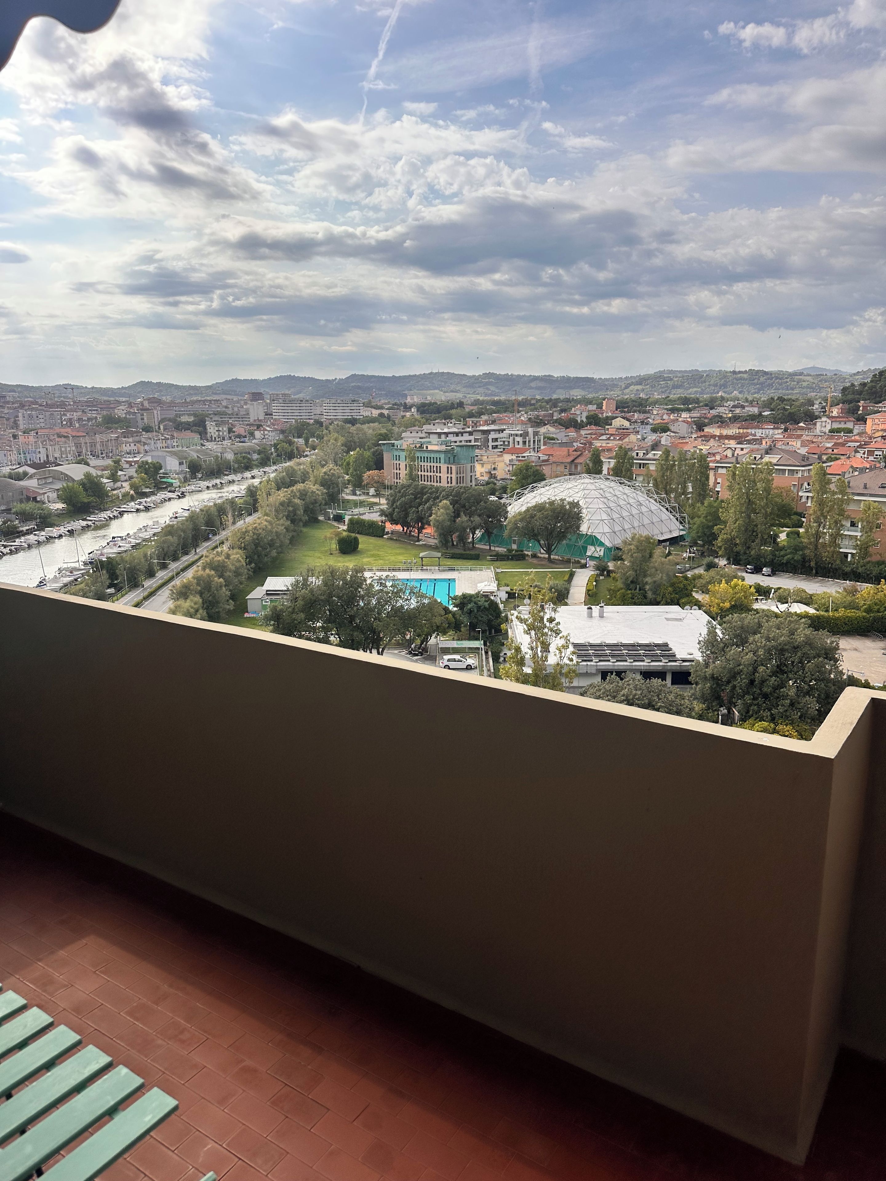 Un balcón con vistas a un paisaje urbano, que incluye un río, edificios y una estructura con forma de cúpula.