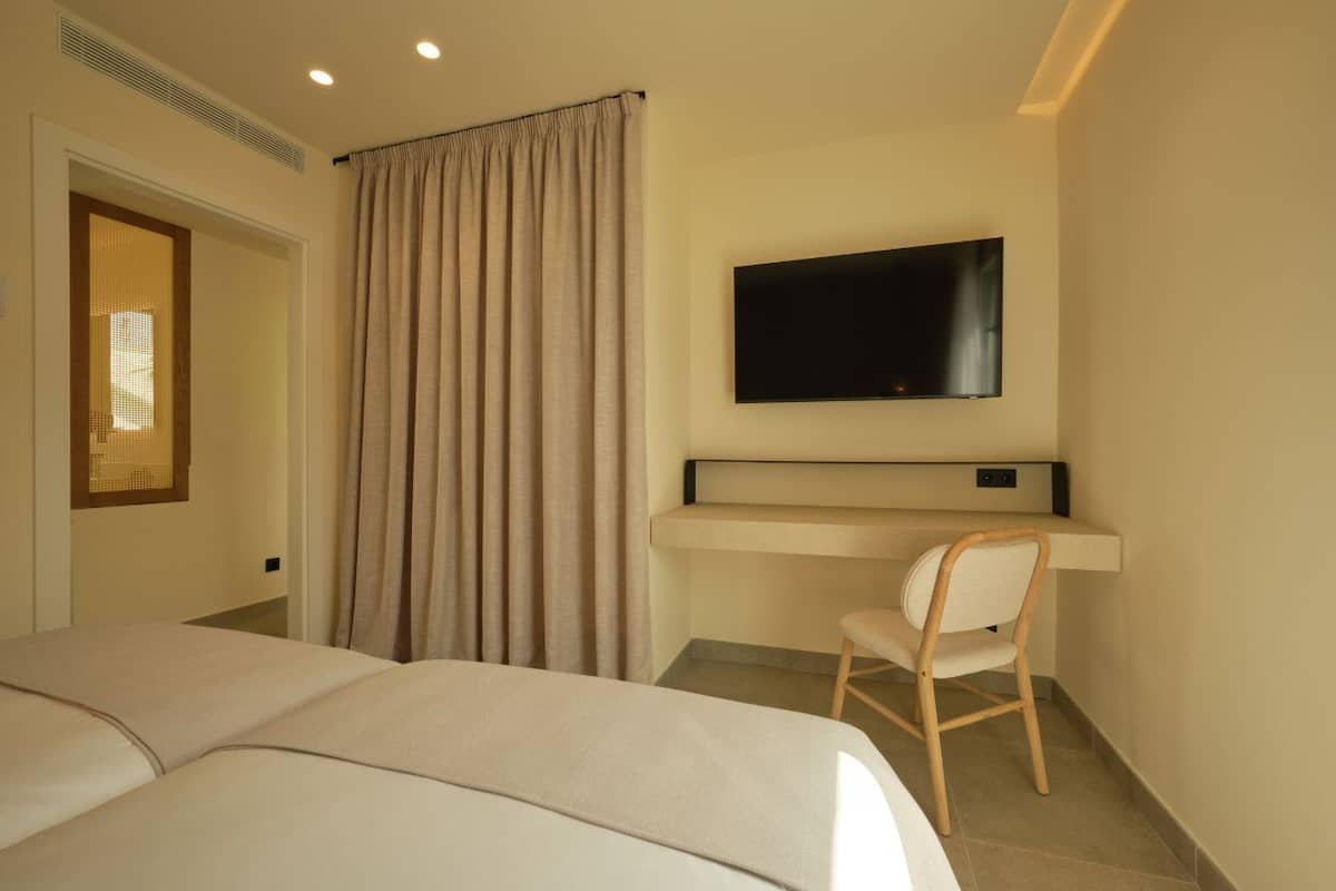 Ein Hotelzimmer mit Bett, Schreibtisch mit Stuhl, einem an der Wand montierten Fernseher und einem Fenster mit Vorhängen.