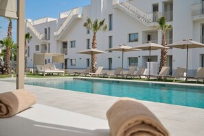 A poolside area with lounge chairs, umbrellas, and a building with balconies. - Belle Playa de Palma Apartsuites (Palma de Mallorca)
