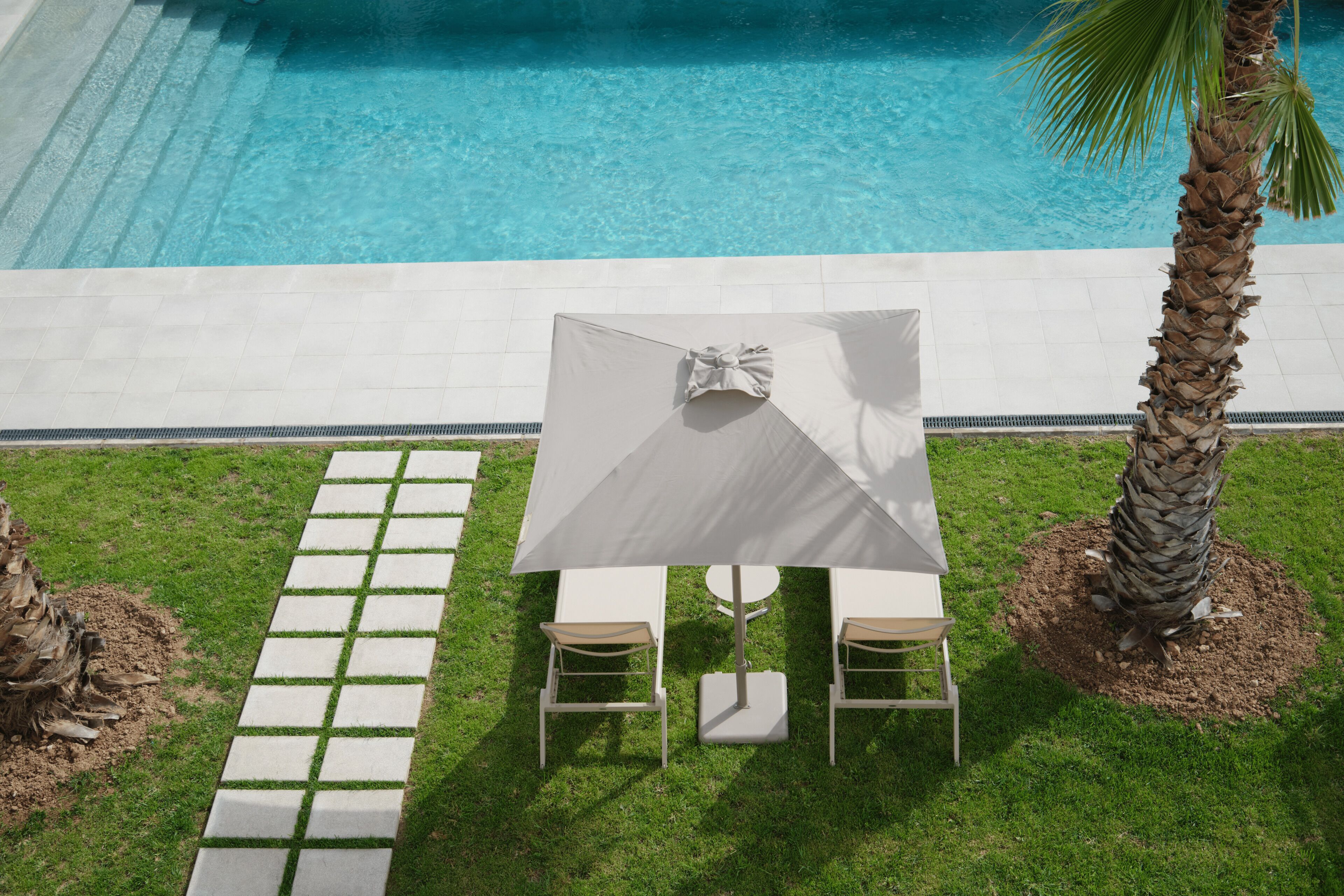 Ein Poolbereich mit Tisch und Stühlen unter einer Markise, umgeben von einer gefliesten Terrasse und Palmen.