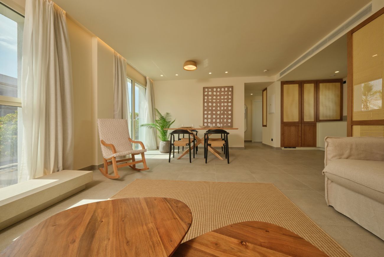 A spacious living area with a wooden coffee table, a sofa, a dining table with chairs, and a potted plant.