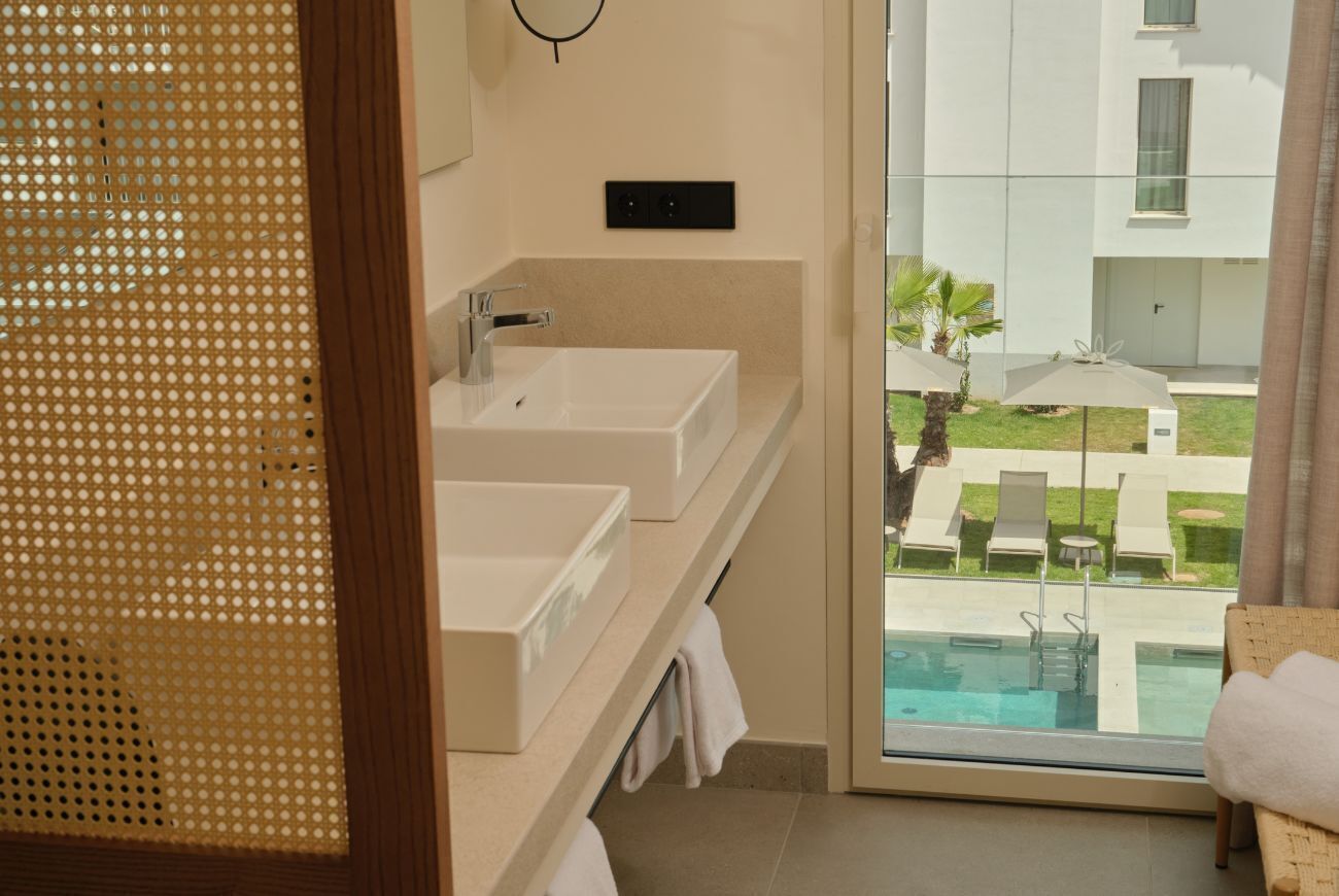 Une salle de bain avec deux lavabos, un miroir et une vue sur l’espace extérieur abritant une piscine.