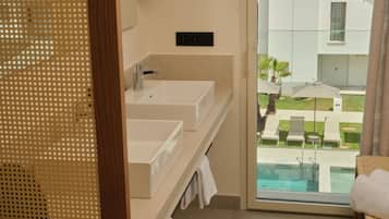 Une salle de bain avec deux lavabos, un miroir et une vue sur l’espace extérieur abritant une piscine.