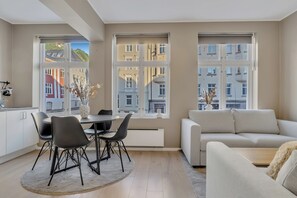 Ein modernes Wohnzimmer mit einer Couch, Esstisch, Stühlen und großen Fenstern mit Blick auf die Stadt.