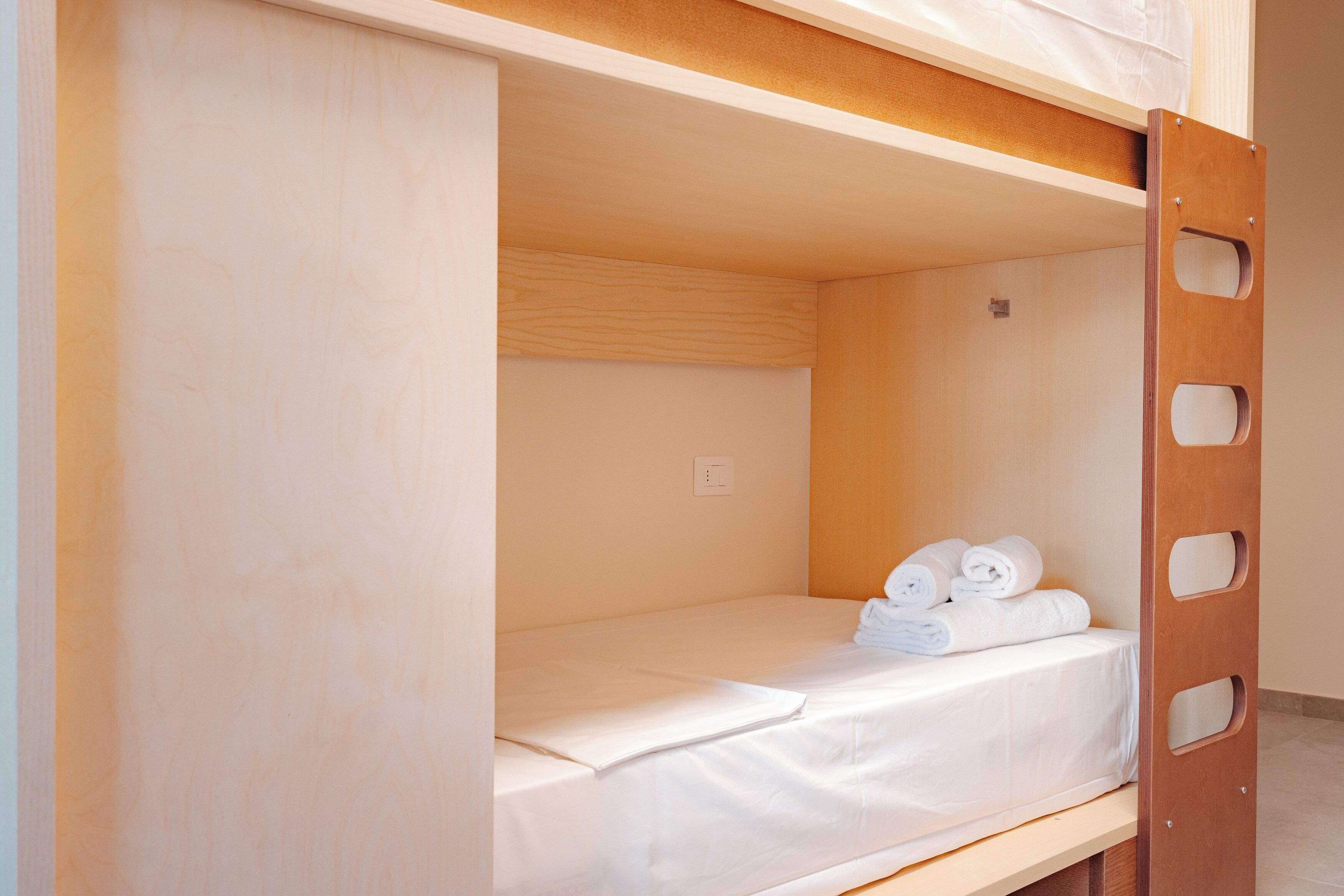 Un lit superposé avec une échelle en bois, un matelas blanc et des serviettes enroulées sur le lit du bas.