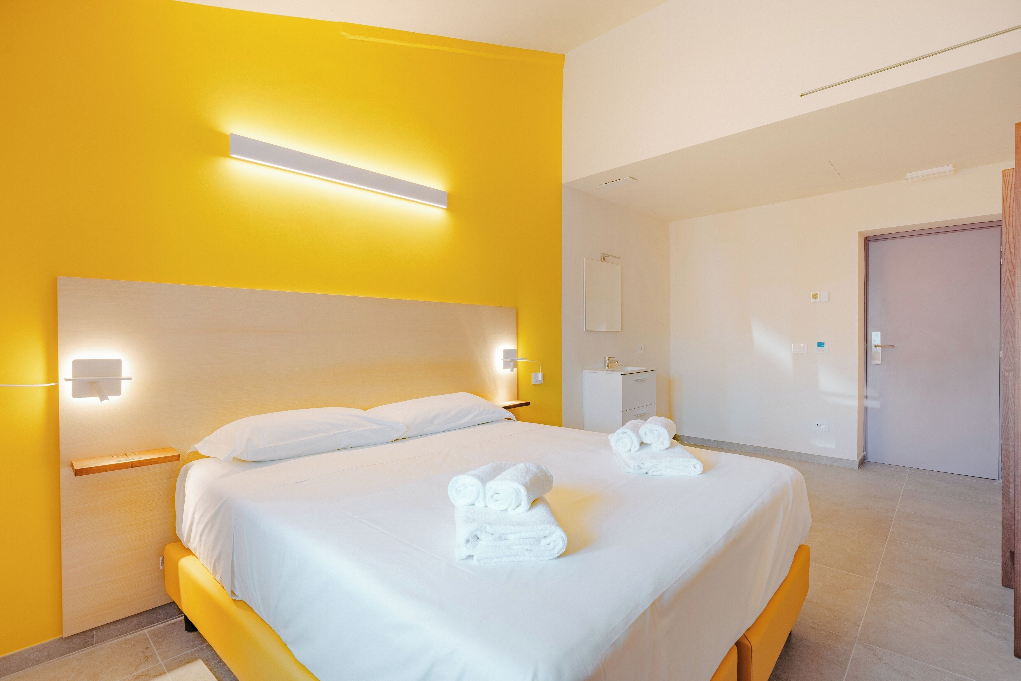 A hotel room with a large bed, bedside tables, a nightstand, a mirror, and a door.
