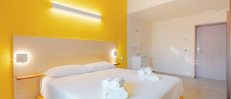 A hotel room with a large bed, bedside tables, a nightstand, a mirror, and a door.