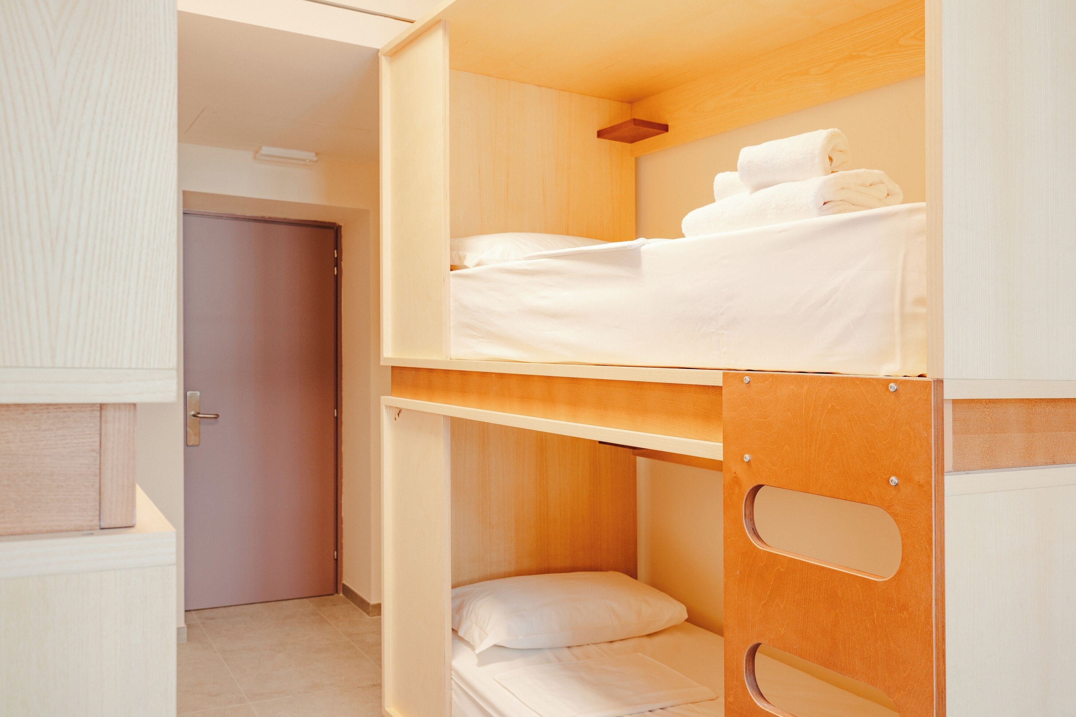 Una cama nido con ropa blanca y cabecera de madera.