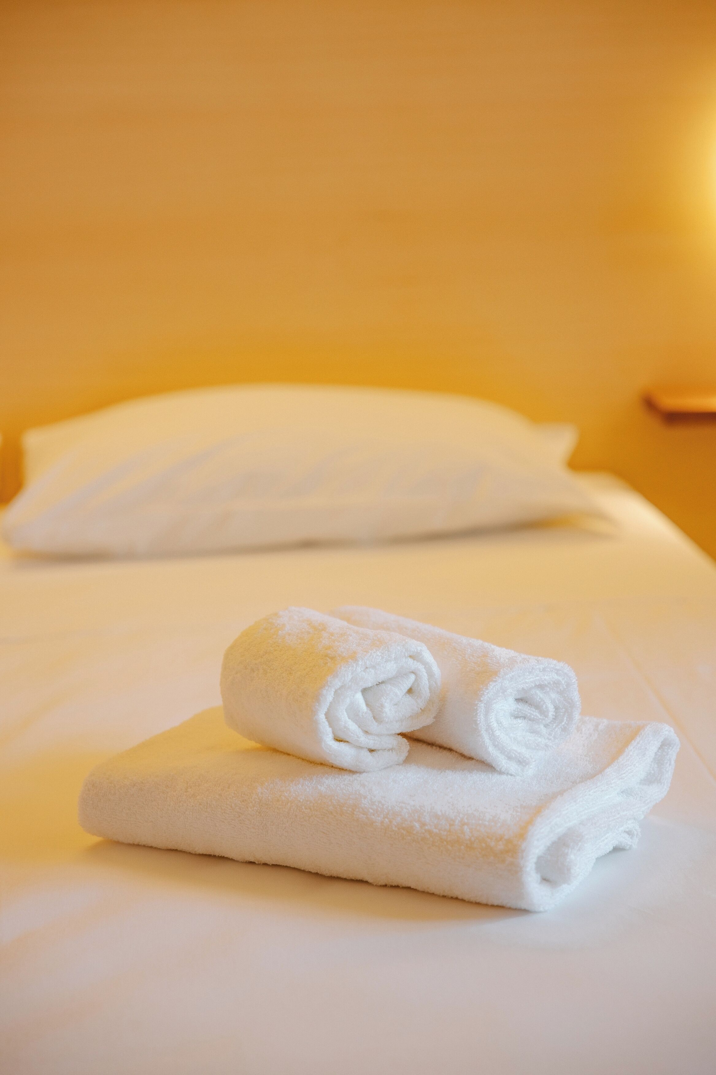 A neatly made bed with white linens and a rolled towel on top.