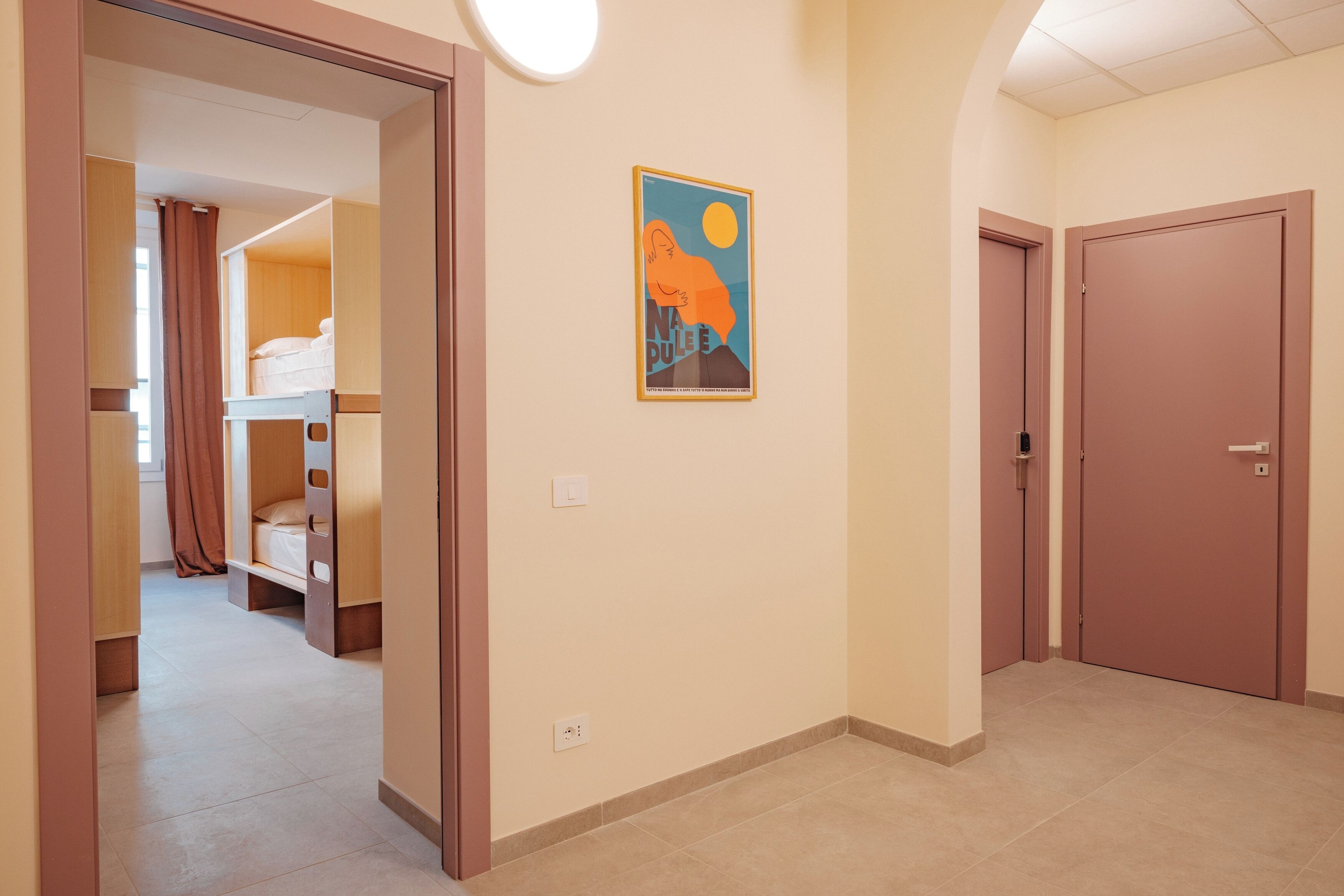 Un couloir avec des lits superposés, une affiche encadrée et des portes fermées.