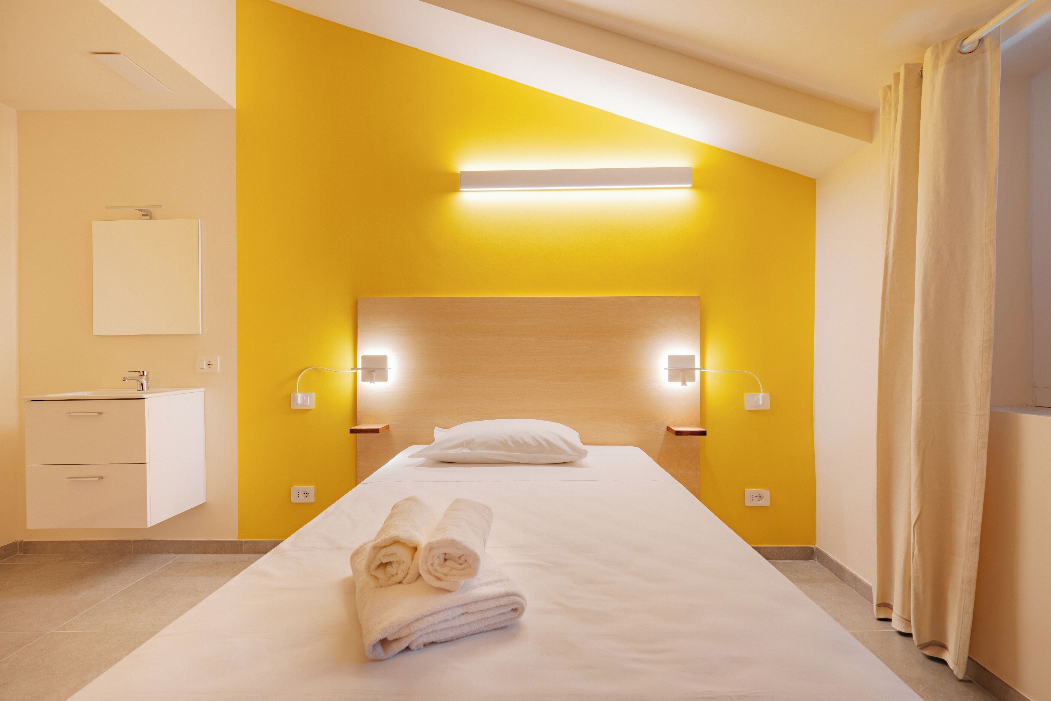 Une chambre d’hôtel comprenant un lit, une table de chevet, une petite table et un luminaire fixé au mur.