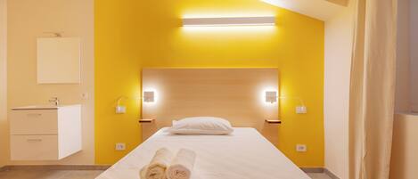 Une chambre d’hôtel comprenant un lit, une table de chevet, une petite table et un luminaire fixé au mur.