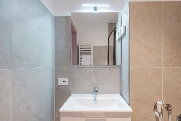 Un baño moderno con lavamanos blanco, espejo y toallero.