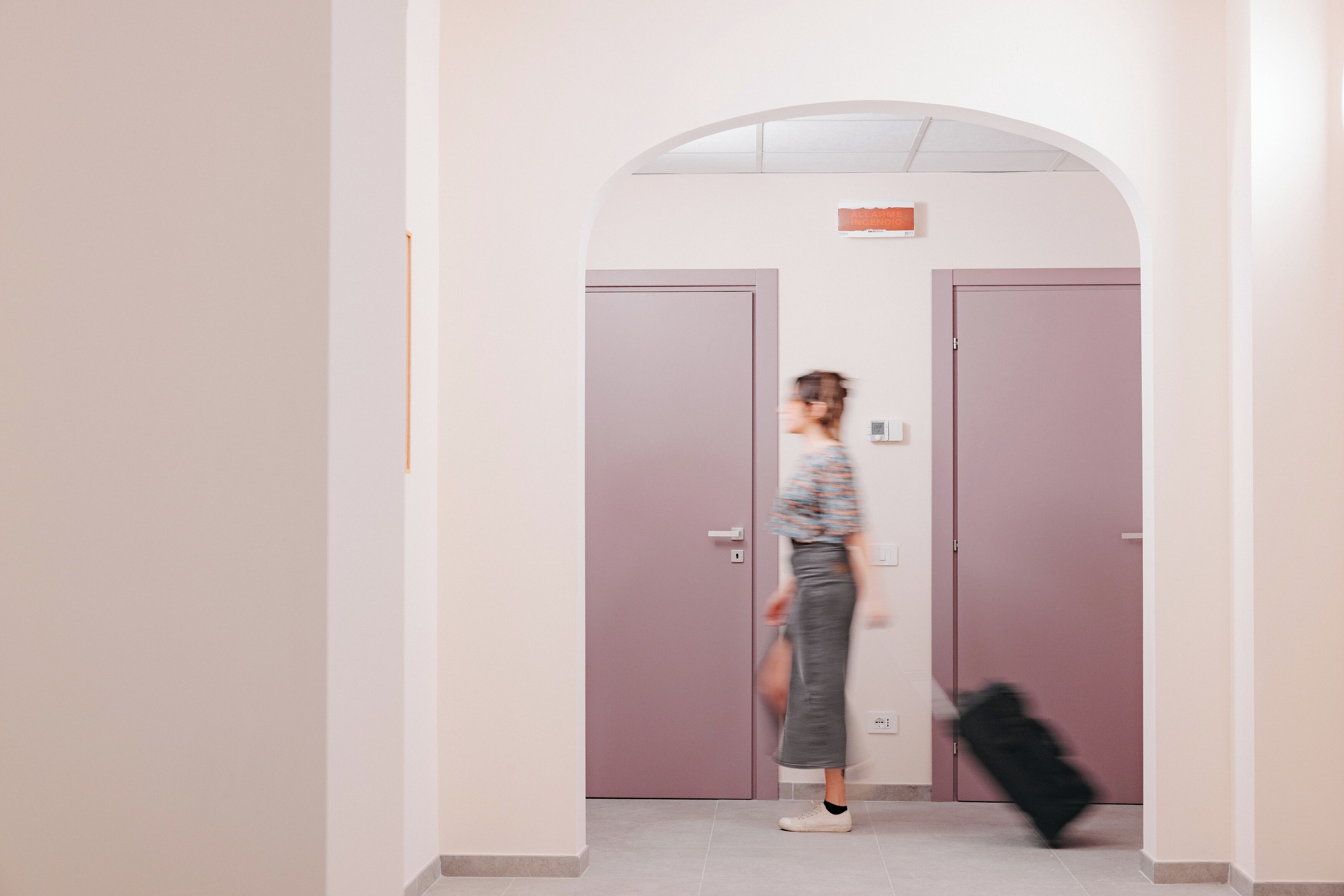 A hallway with a door, a person walking, and a suitcase.