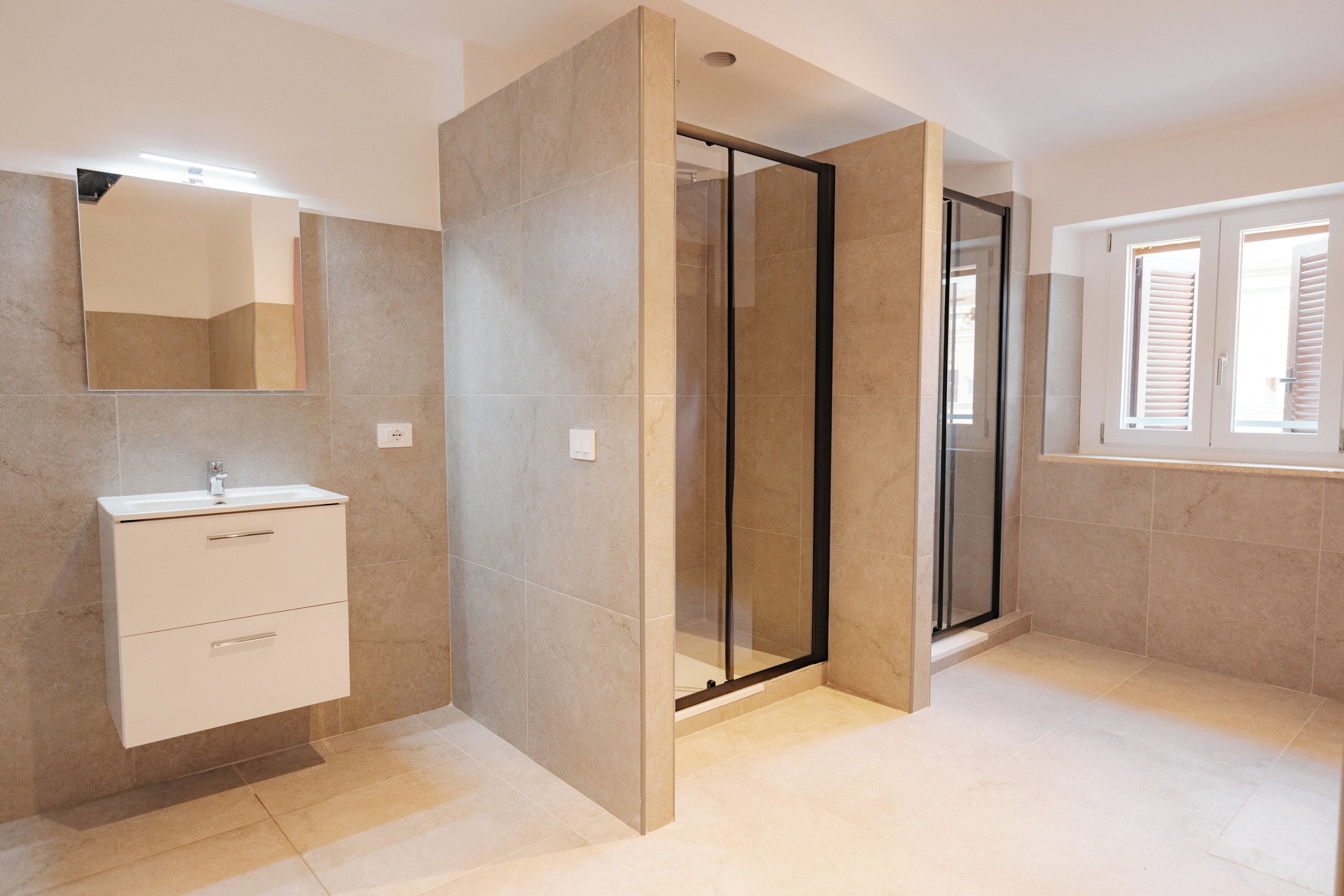 A modern bathroom with a glass shower enclosure, a vanity with drawers, and a window with blinds.