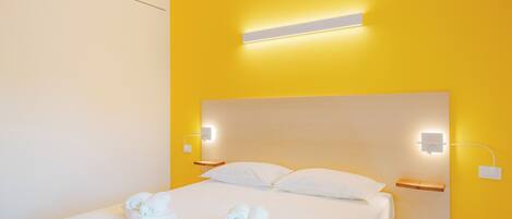 A hotel room with a bed, white linens, two wall-mounted light fixtures, and a bedside table.