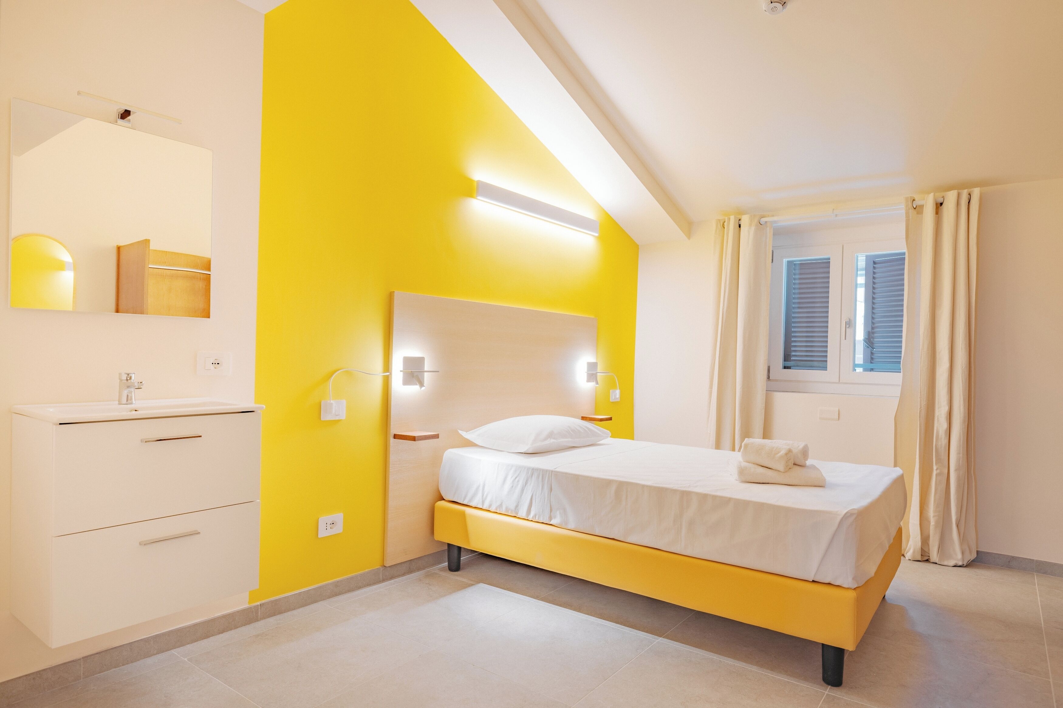 Een slaapkamer met een bed, nachtkastje, spiegel en een raam met gordijnen.