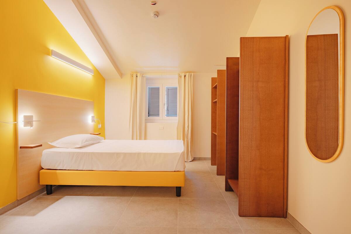 A hotel room with a bed, bedside tables, a wardrobe, and a mirror.
