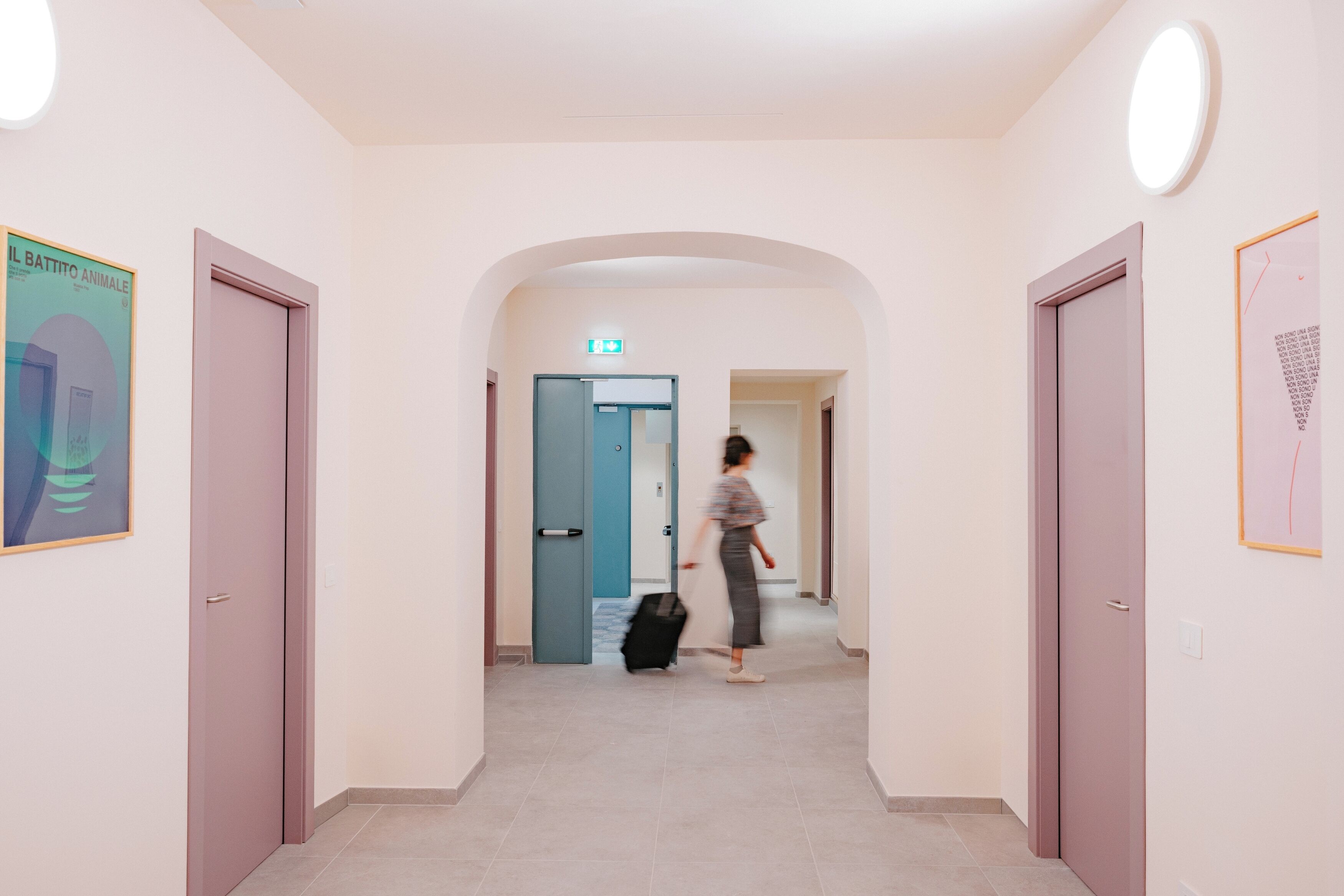 A hallway with doors, a blue door, and a person with a suitcase.