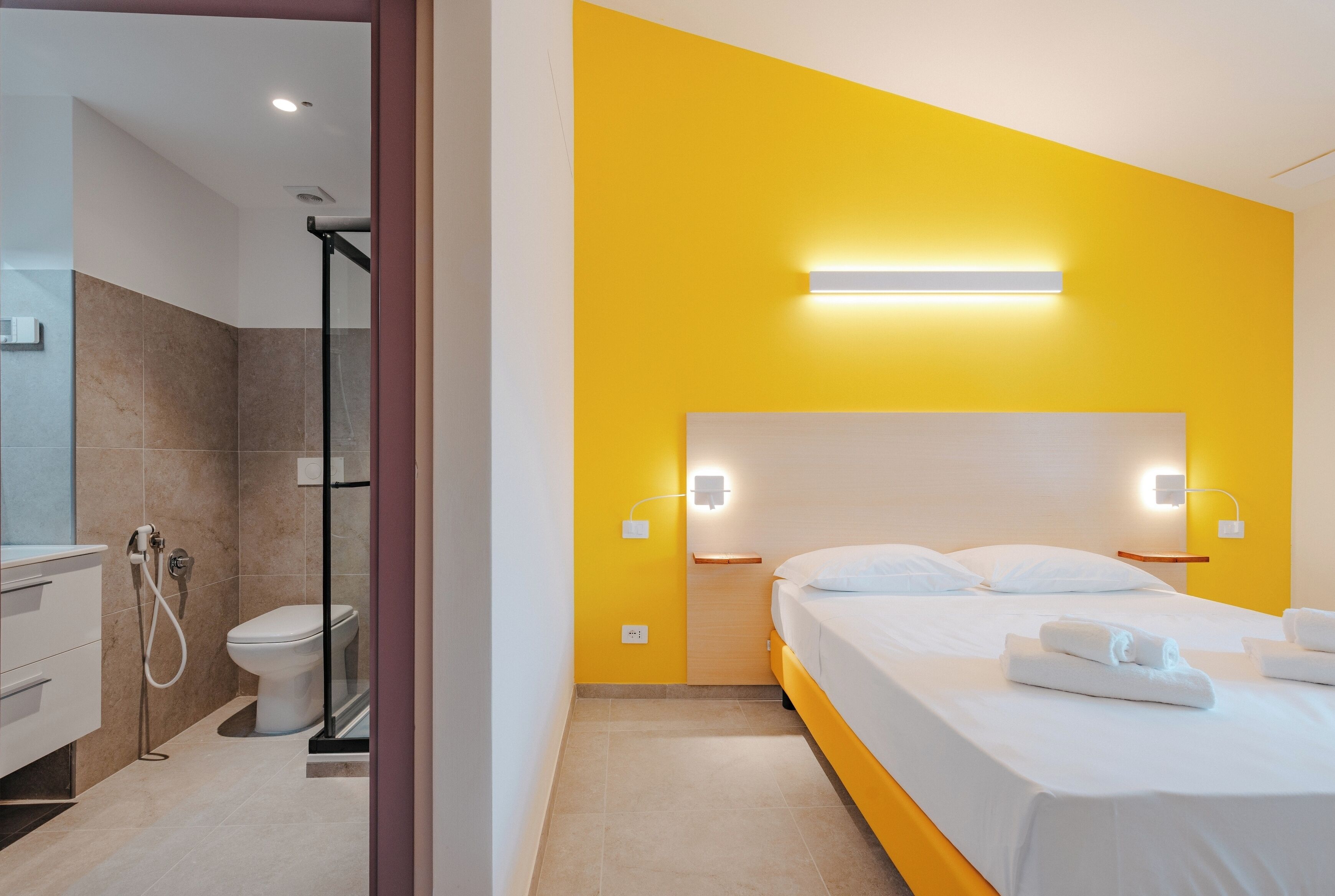 Quarto de hotel com chuveiro, vaso sanitário, cama e mesas de cabeceira.