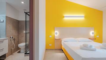 Quarto de hotel com chuveiro, vaso sanitário, cama e mesas de cabeceira.