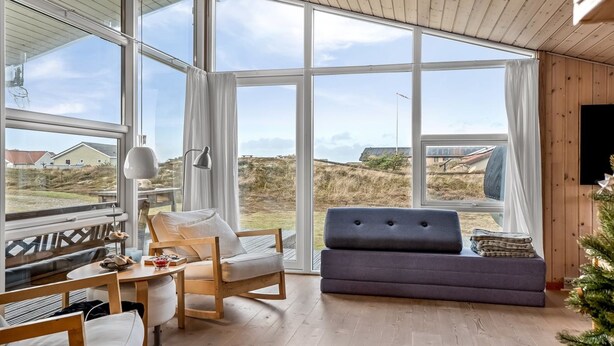 Een moderne woonkamer met grote ramen, een bank, een fauteuil en een bijzettafeltje.