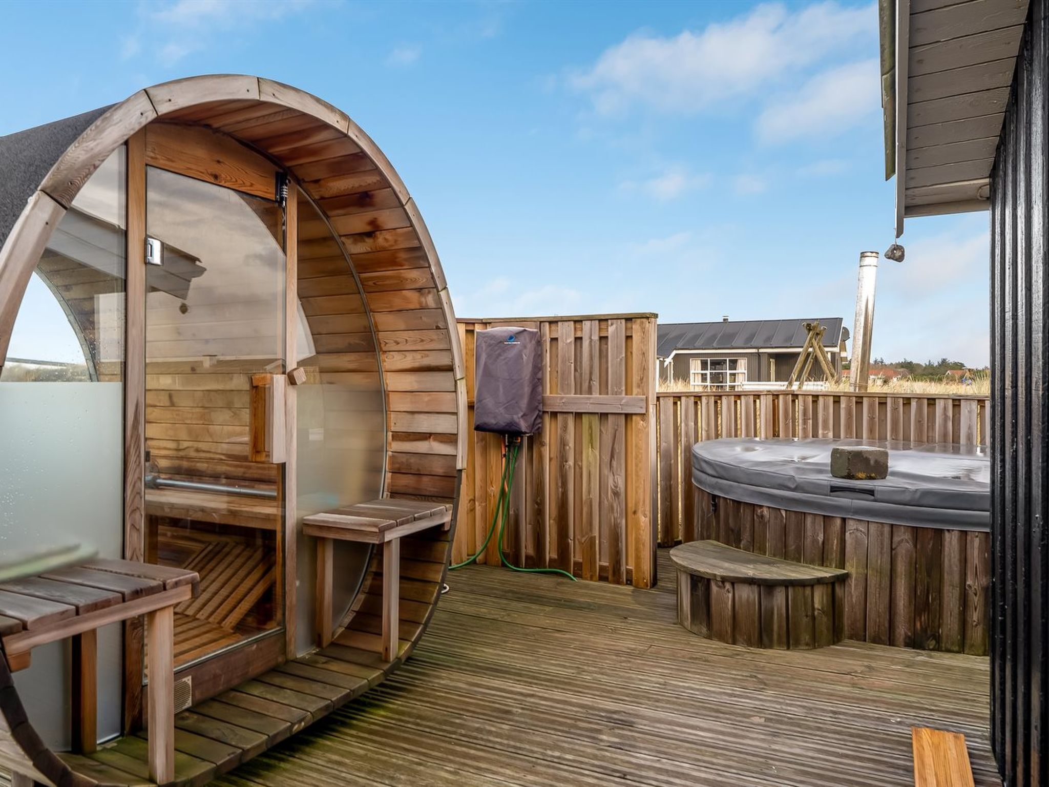 Un espace aménagé avec un bain à remous en bois, doté d’une structure en bois aux lignes courbes, d’une terrasse en bois et du bain à remous lui-même.