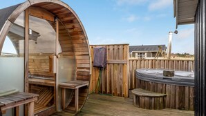 Een houten kuub met een gebogen houten constructie, een houten terras en een jacuzzi.