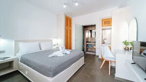 Una habitación de hotel moderna con cama, mesita de noche, televisor y baño visible a través de una puerta abierta.