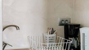 Una cocina con un lavamanos blanco, una cafetera y una cesta blanca con utensilios.