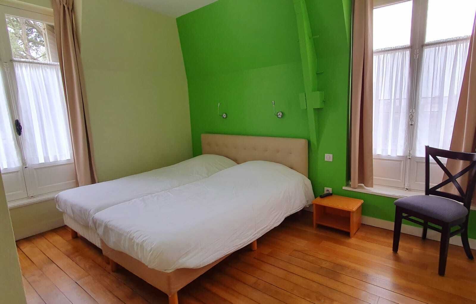 A bedroom with a bed, a nightstand, a chair, and a window with curtains.