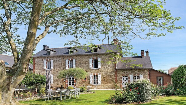 Une maison en pierre avec un jardin, un coin repas et un grand arbre.
