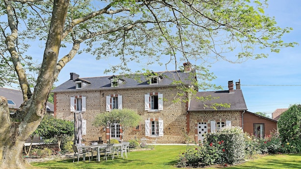 Una casa de piedra con jardín, comedor y un gran árbol.