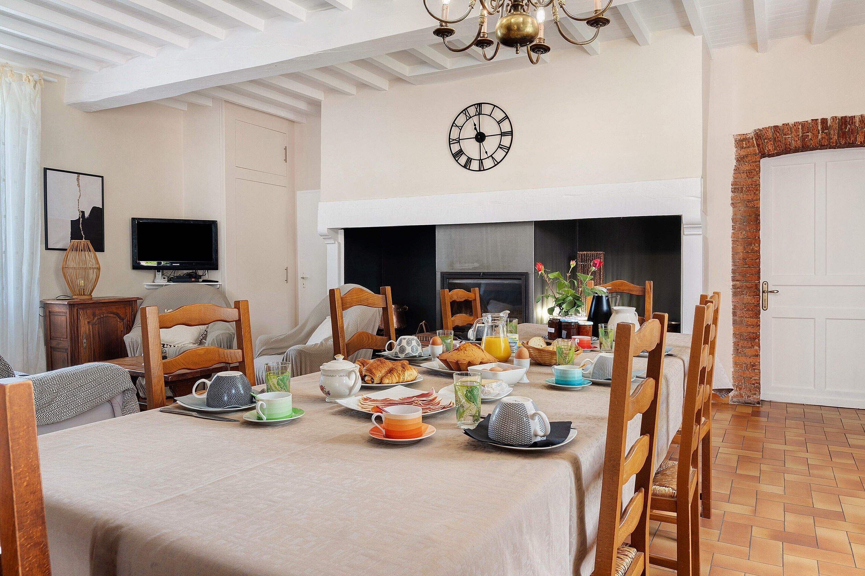 A dining area with a table set for breakfast, a clock on the wall, and a fireplace.