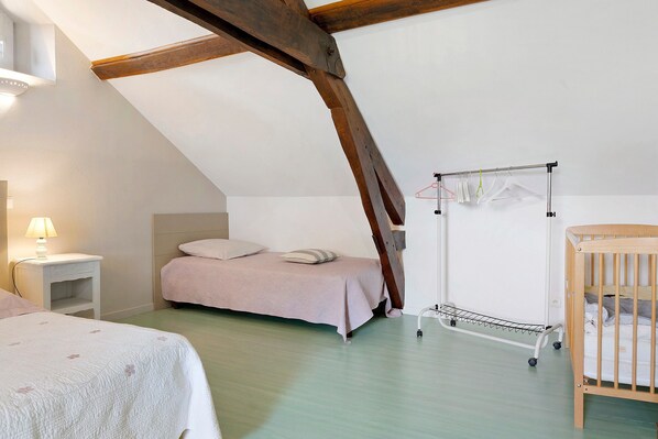 Ein Schlafzimmer mit schrägem Dach, einem Babybett, einem Bett, einem Nachttisch und einem Wäscheständer.