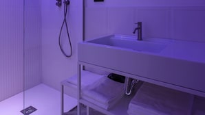A modern bathroom with a glass-enclosed shower, a white sink, and a mirror above the sink. - Deluxe Room 101 in the heart of Naples! (NAPOLI)