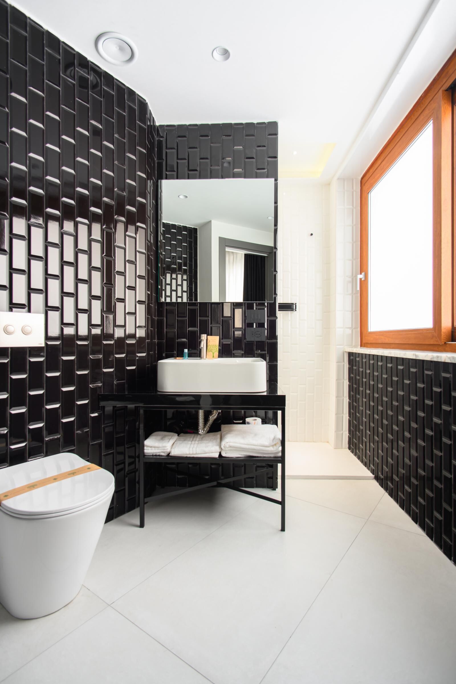 A modern bathroom with a black and white tiled wall, a white sink, and a mirror above it.